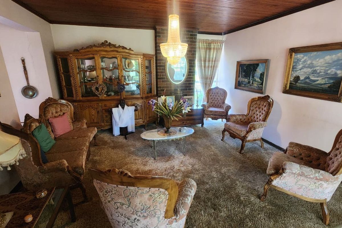 A traditional living room featuring a brick fireplace, timber ceiling, and carpeted flooring, offering a classic layout with potential for modern updates.