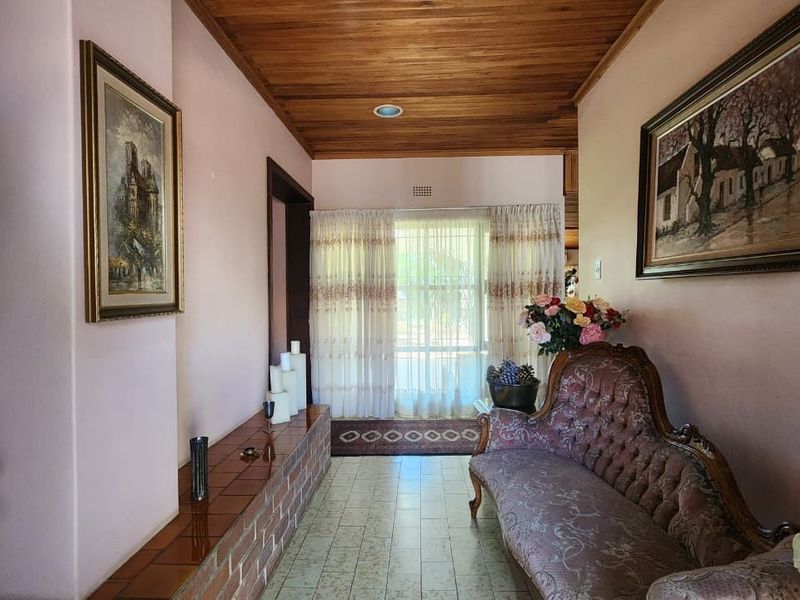 A spacious hallway featuring a warm timber ceiling, tiled flooring, and a built-in brick feature ledge, leading towards a bright windowed entrance.