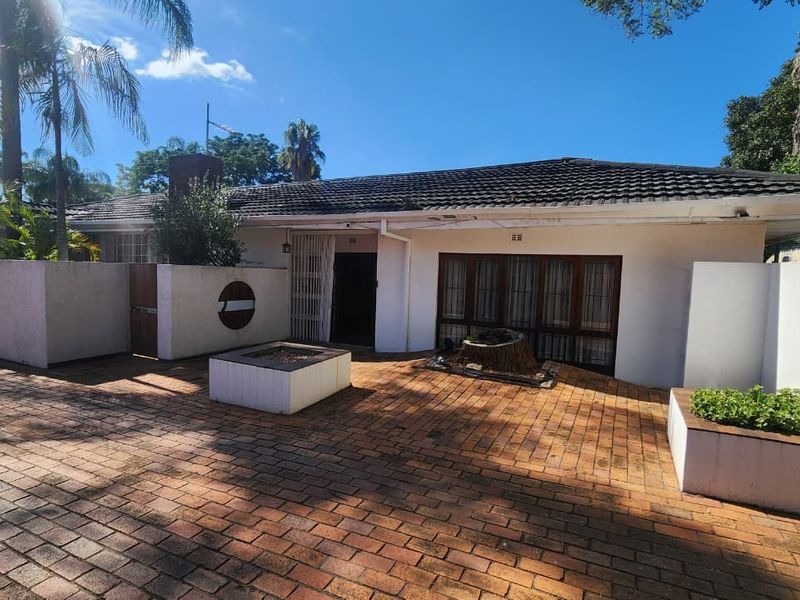 Front exterior view of a single-story house featuring a brick-paved courtyard, security gate, and built-in planter boxes under a tiled roof.