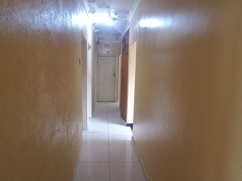 A narrow residential hallway featuring tiled flooring and requiring ceiling and wall maintenance.