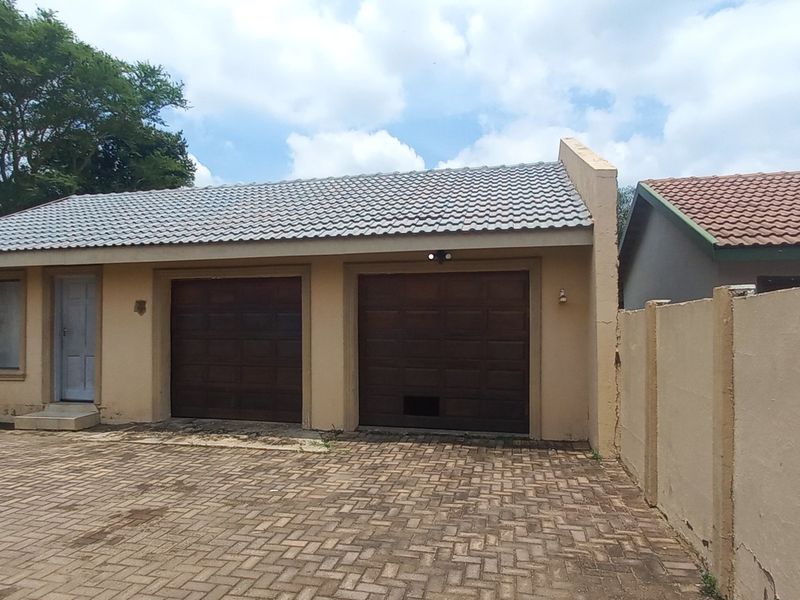 A detached double garage featuring a tiled roof, paved driveway, and perimeter walling, showing signs of exterior wear.