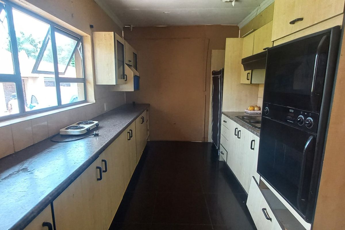 A galley-style kitchen featuring built-in cabinetry, integrated oven, and extractor fan, requiring cosmetic updates to modernize the dated finishes.