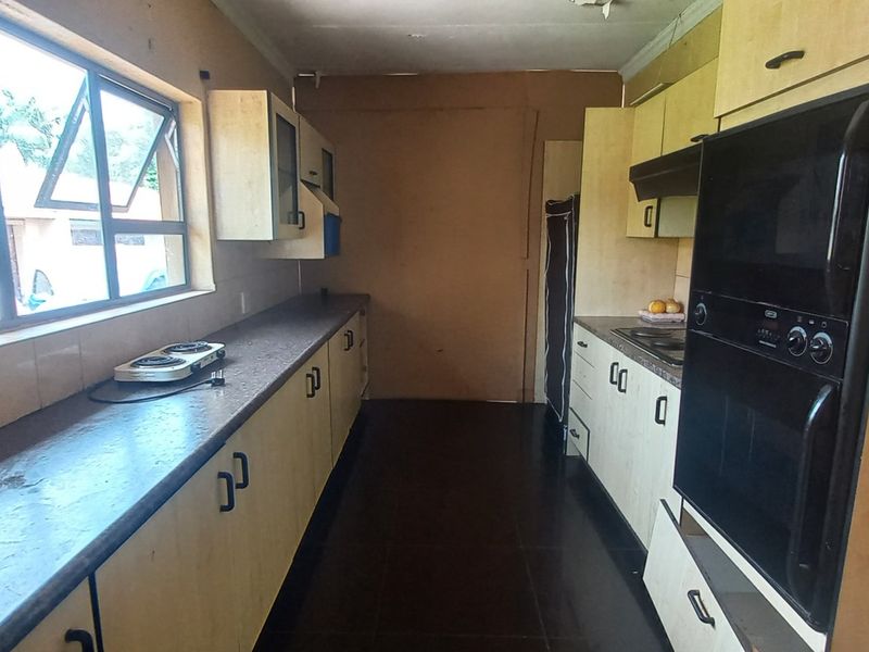 A galley-style kitchen featuring built-in cabinetry, integrated oven, and extractor fan, requiring cosmetic updates to modernize the dated finishes.
