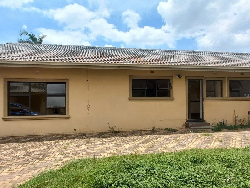Rear elevation of a single-story house featuring a tiled roof, paved driveway, and aluminium window frames, showing signs of exterior wear.