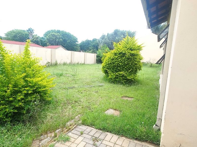 A view of the rear garden area featuring a paved walkway, lawn, and perimeter boundary wall.