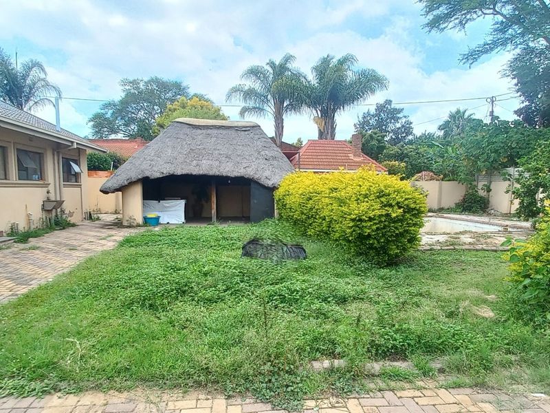 Rear garden area featuring a thatched lapa, paved surfaces, and a swimming pool, requiring landscaping and maintenance to restore its appeal.