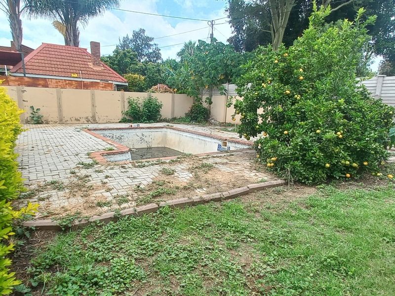 Outdoor pool area featuring a swimming pool with surrounding paving and boundary walling, currently requiring significant maintenance and landscaping.