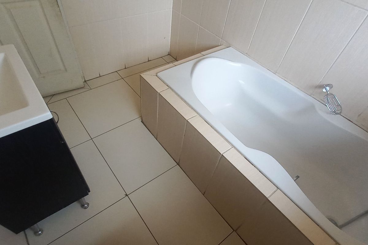 A functional bathroom featuring a built-in bathtub and a vanity basin with tiled walls and flooring throughout.
