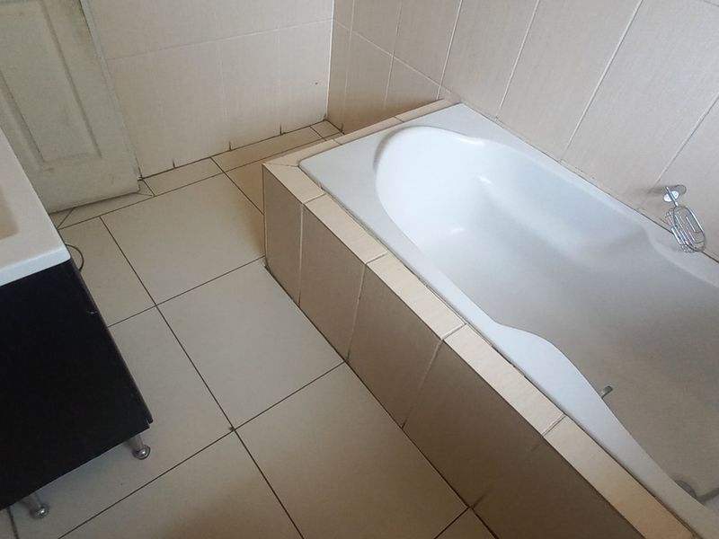 A functional bathroom featuring a built-in bathtub and a vanity basin with tiled walls and flooring throughout.