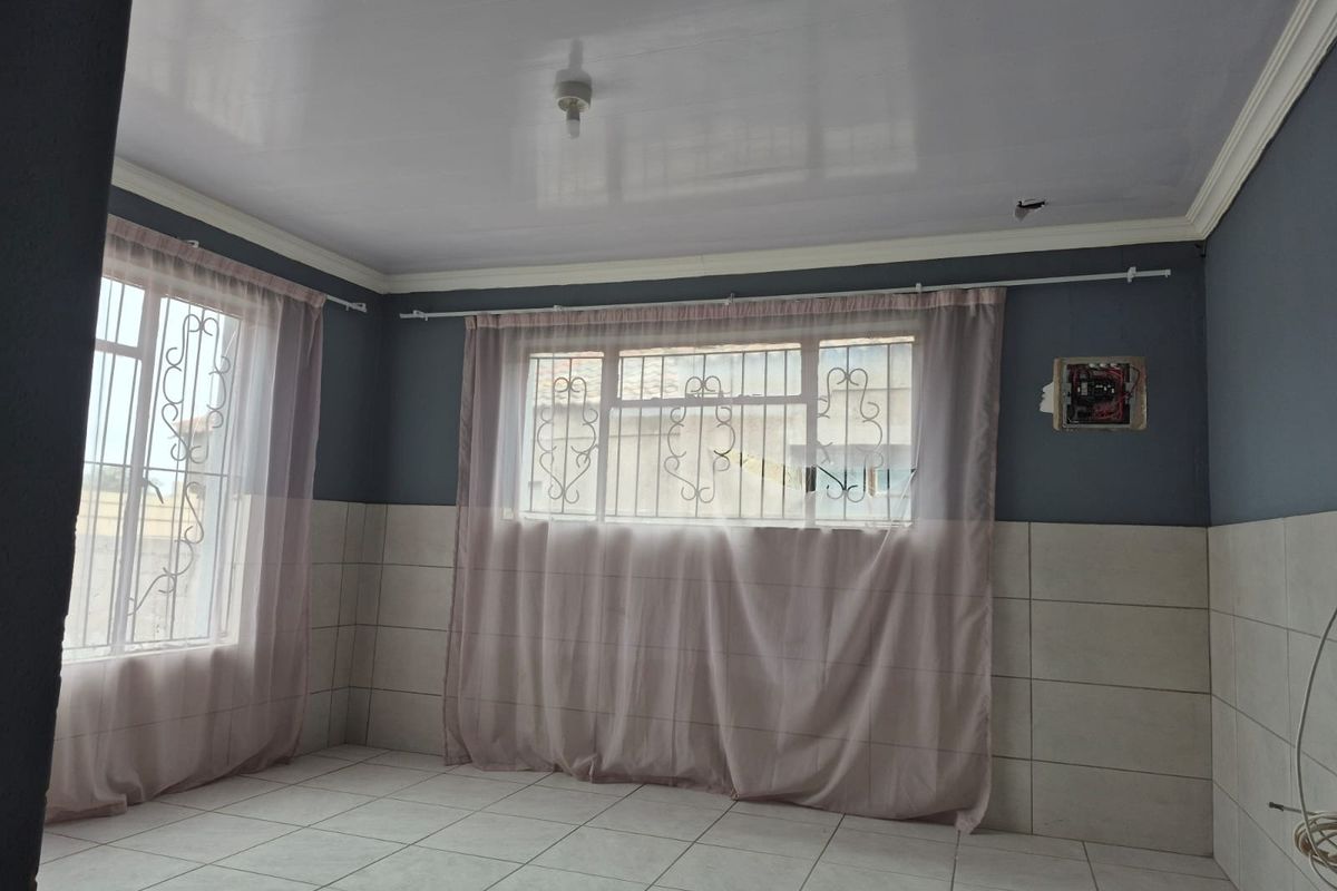 An empty living area featuring tiled floors, half-wall tiling, and security bars on windows, requiring minor electrical repairs and finishing touches.