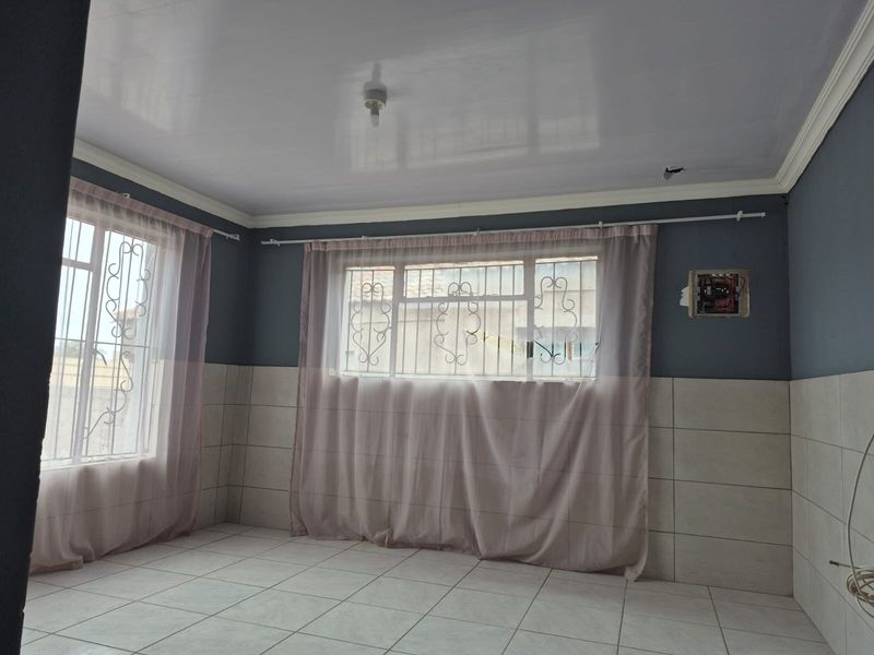 An empty living area featuring tiled floors, half-wall tiling, and security bars on windows, requiring minor electrical repairs and finishing touches.
