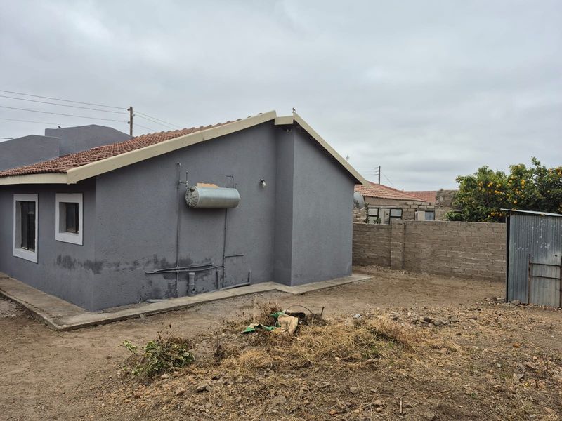 Rear view of the property featuring a plastered exterior, external geyser, concrete boundary wall, and a small metal storage shed in the yard.
