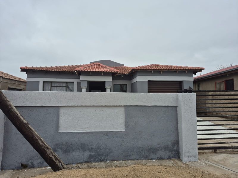 Front view of a single-story house featuring a tiled roof, perimeter wall with gate, and integrated garage.