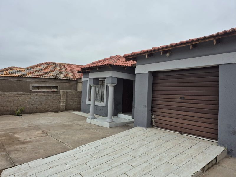 Front view of a single-story house featuring a tiled roof, roller garage door, paved driveway, and a small covered entrance porch with decorative columns.