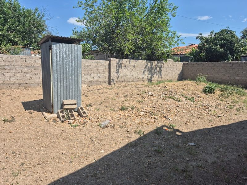 A large, undeveloped backyard area featuring a concrete block perimeter wall and a basic corrugated metal outdoor structure.