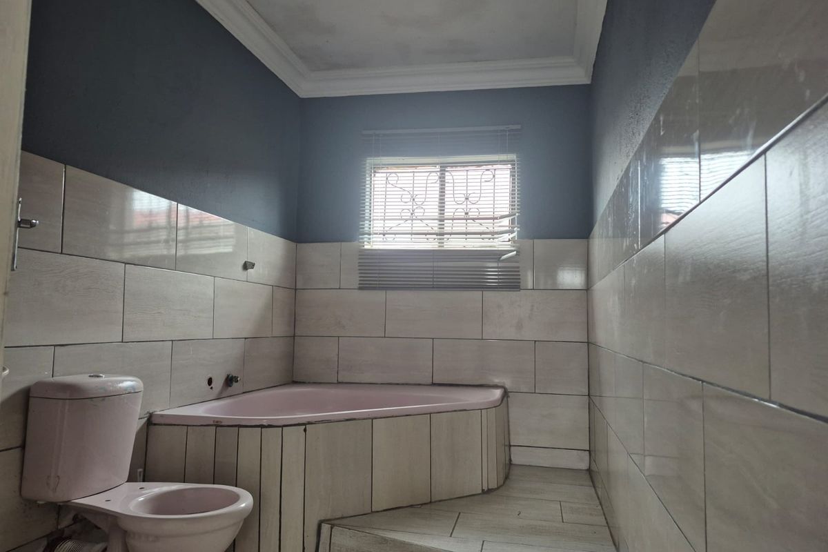 A spacious bathroom featuring a corner bathtub and toilet, with neutral wall tiling and dark painted upper walls, requiring some cosmetic updates.
