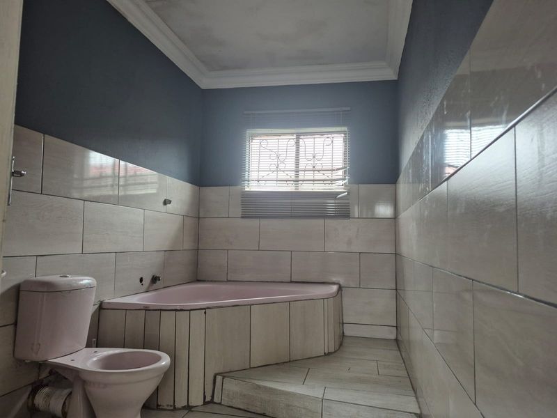 A spacious bathroom featuring a corner bathtub and toilet, with neutral wall tiling and dark painted upper walls, requiring some cosmetic updates.
