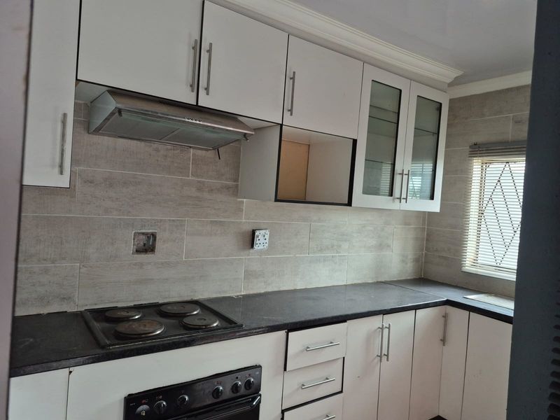 A functional kitchen featuring white cabinetry, dark stone countertops, a built-in oven and hob, and a tiled backsplash.