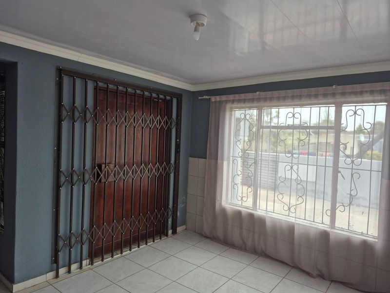 An empty living area featuring tiled flooring, a security gate, and window security bars, providing a functional space ready for personalization.