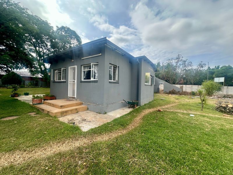 Rear view of a detached house featuring a concrete patio, security gate, and casement windows set within a large garden area.