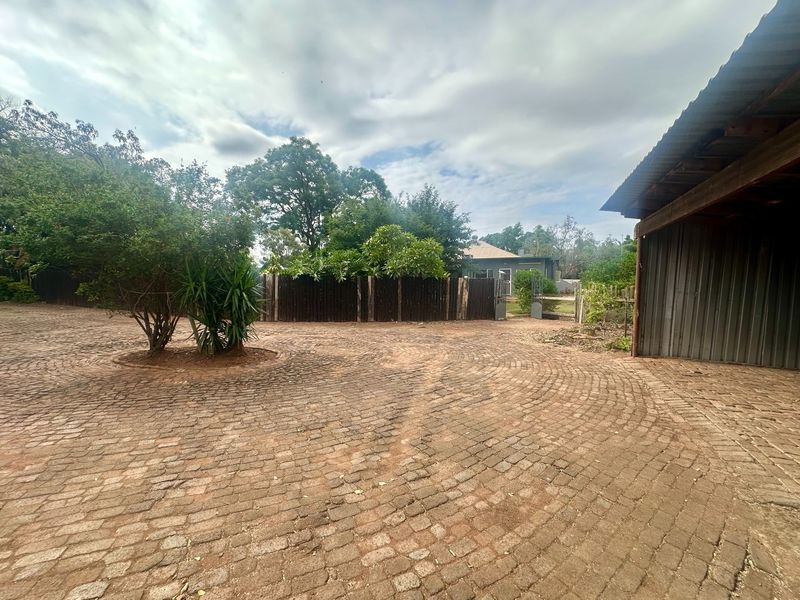 Spacious front driveway featuring circular cobblestone paving, a corrugated metal carport, and secure perimeter fencing.