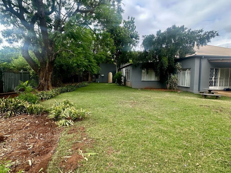 A spacious rear garden featuring a large lawn, mature trees, and a view of the house exterior with a covered patio area.