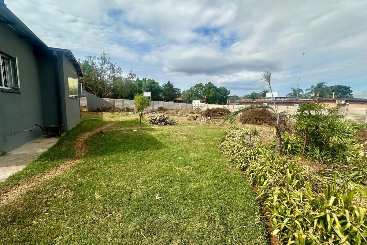 A spacious rear garden area featuring a lawn, established garden beds, and a secure precast concrete boundary wall.