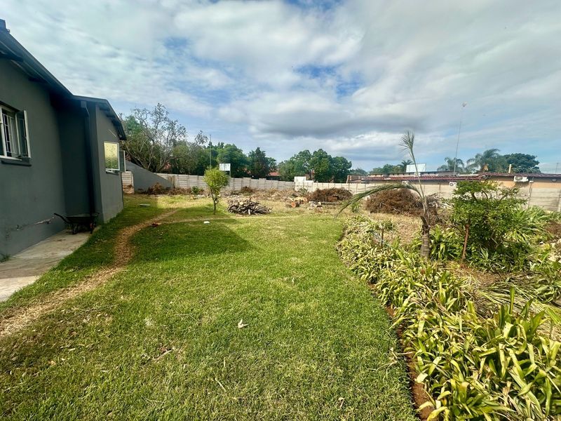A spacious rear garden area featuring a lawn, established garden beds, and a secure precast concrete boundary wall.