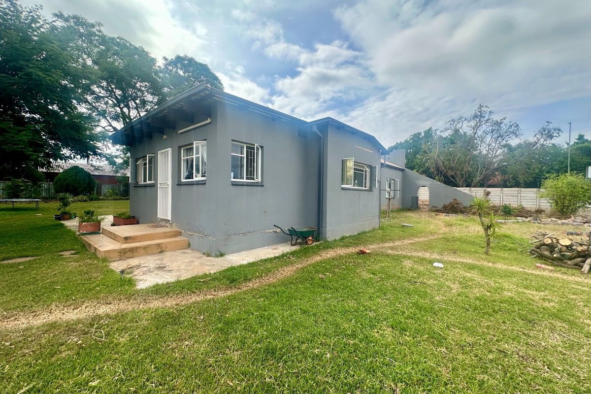 Rear view of a detached house featuring a concrete patio, security gate, and casement windows set within a large, grassed garden area.