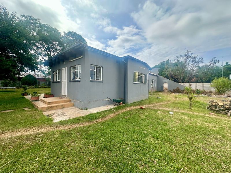 Rear view of a detached house featuring a concrete patio, security gate, and casement windows set within a large, grassed garden area.