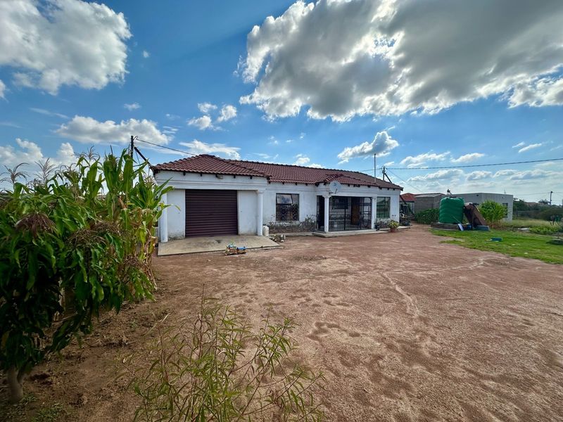 Front view of a single-story house featuring a tiled roof, integrated garage with a roller door, and a large unpaved yard area.