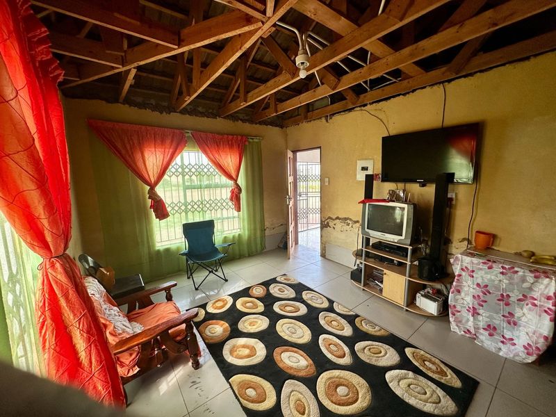Living room featuring exposed timber roof trusses, tiled flooring, and security fixtures, requiring cosmetic updates to the wall finishes.