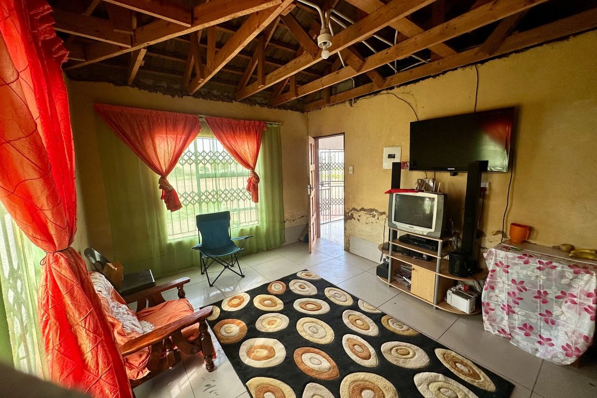 Living room featuring exposed timber roof trusses, tiled flooring, and security fixtures, requiring cosmetic updates to the wall finishes.