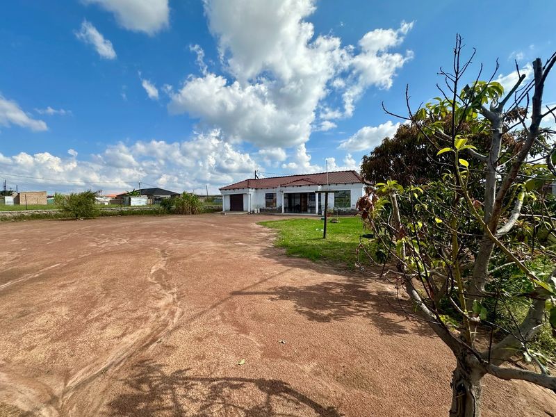 A view of the rear exterior of the house featuring a large unpaved yard area and a tiled roof structure.