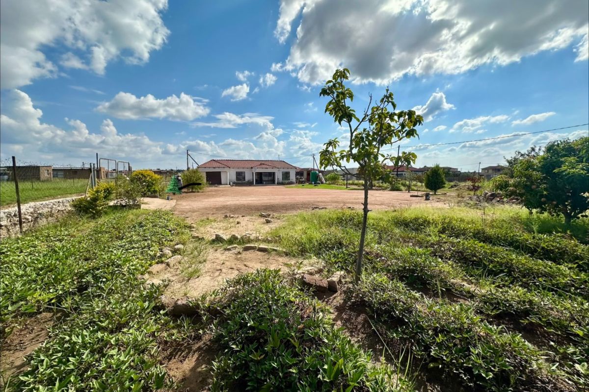 A wide-angle view of the rear exterior of the property, featuring a large, unlandscaped garden area and perimeter fencing.