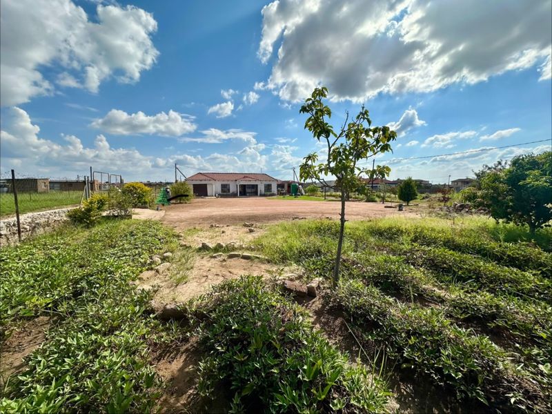 A wide-angle view of the rear exterior of the property, featuring a large, unlandscaped garden area and perimeter fencing.