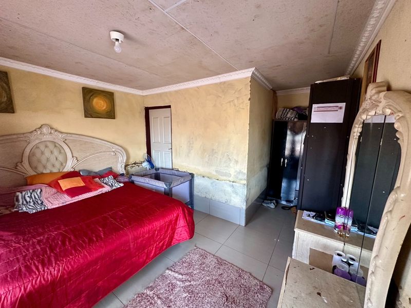 A bedroom featuring tiled flooring and ceiling cornicing, currently showing significant signs of wall dampness, peeling paint, and ceiling staining requiring maintenance.