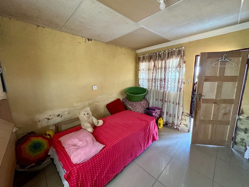 A bedroom featuring tiled flooring and a timber door, currently requiring significant wall repairs and cosmetic updates to improve the overall condition.