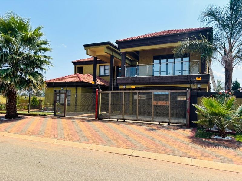 A double-story residential property featuring a paved driveway, secure sliding gate, electric fencing, and an upper-level balcony with a glass balustrade.