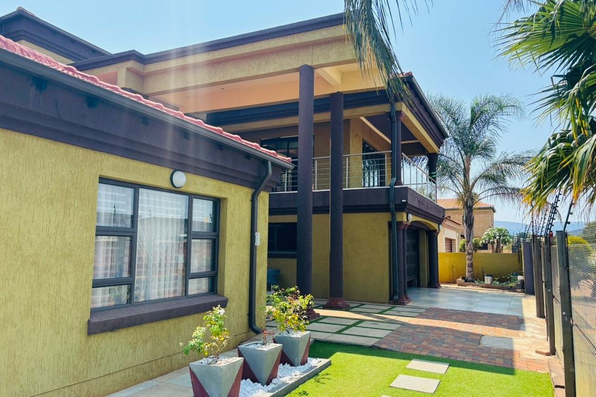 A well-maintained double-story residential exterior featuring a balcony with stainless steel balustrades, paved driveway, and secure electric fencing.