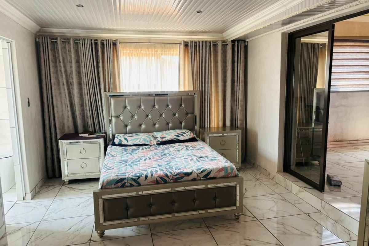 A spacious bedroom featuring polished marble-look floor tiles, recessed ceiling lighting, and a sliding glass door providing access to an adjacent area.