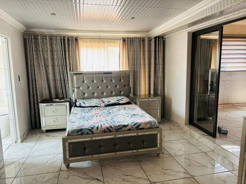 A spacious bedroom featuring polished marble-look floor tiles, recessed ceiling lighting, and a sliding glass door providing access to an adjacent area.