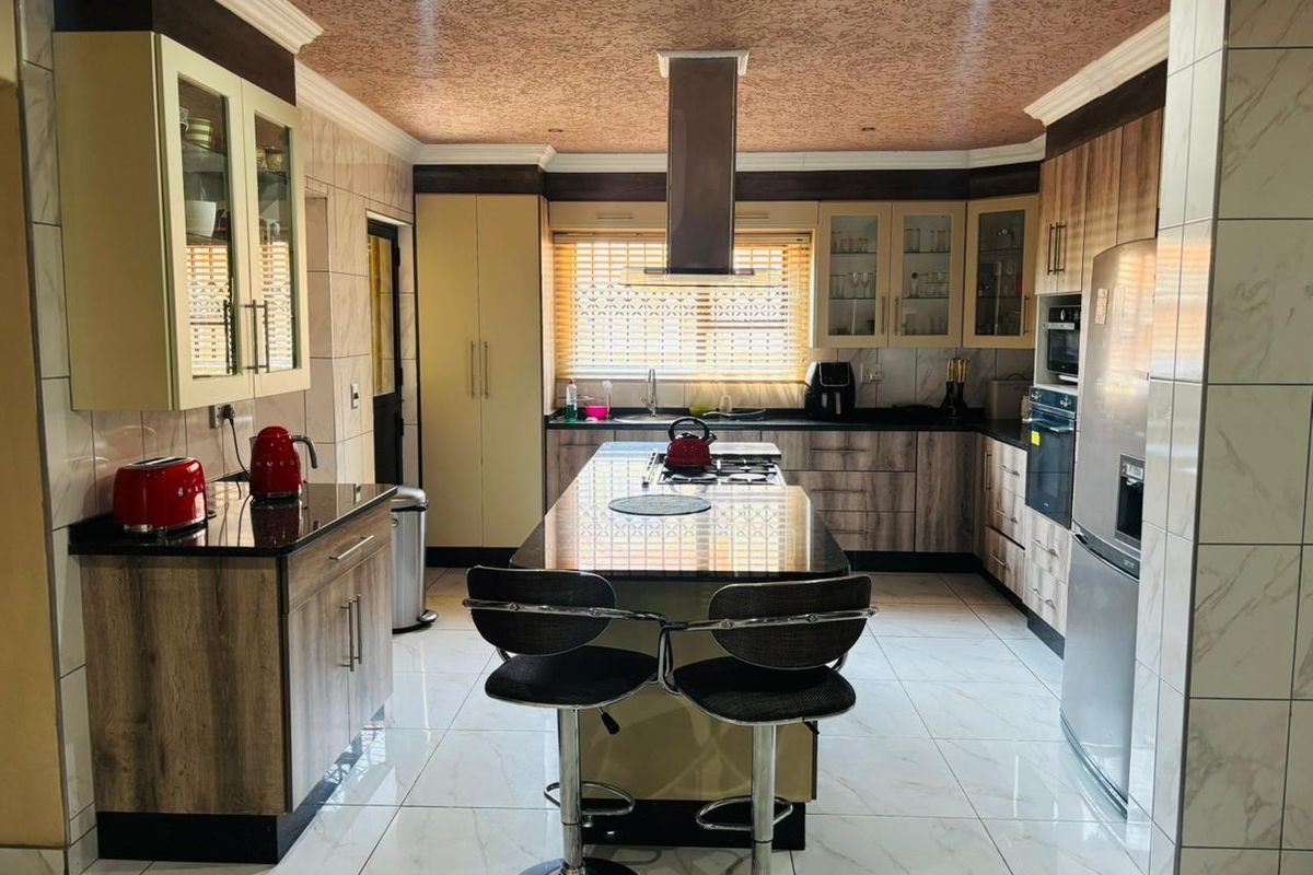 A well-appointed kitchen featuring a central island with a built-in cooktop, granite countertops, ample cabinetry, and modern tiled flooring.