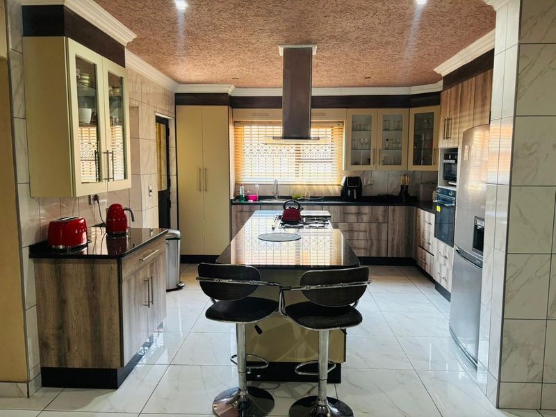 A well-appointed kitchen featuring a central island with a built-in cooktop, granite countertops, ample cabinetry, and modern tiled flooring.