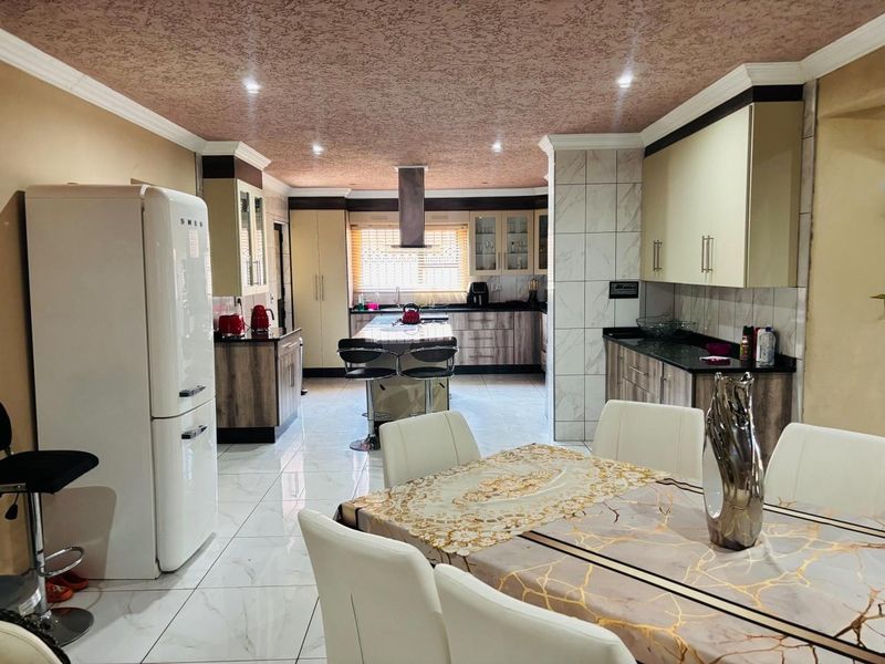 Spacious open-plan kitchen and dining area featuring modern cabinetry, a central island with breakfast bar, and polished tiled flooring throughout.