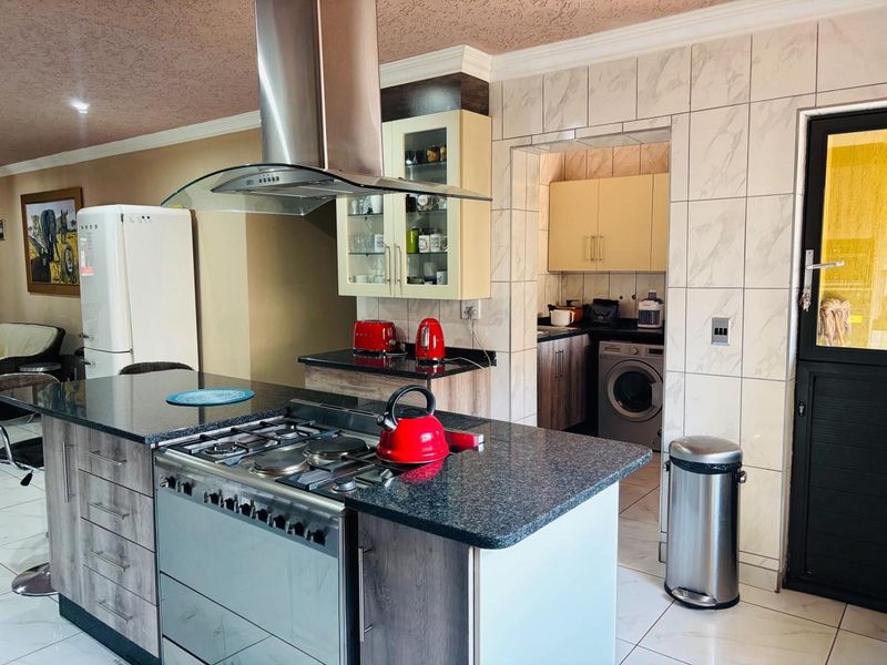 Modern kitchen featuring a central island with a gas stove, extractor fan, granite countertops, and an adjoining scullery area with laundry facilities.