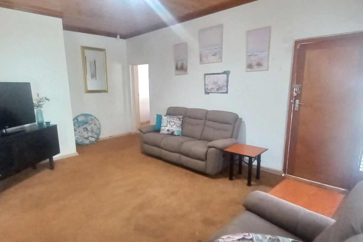 A living room featuring timber ceiling panels, carpeted flooring, and a secure entrance door with a security gate.