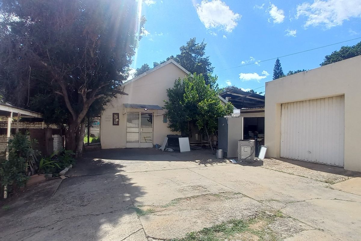 Rear exterior view showing a concrete driveway, double garage doors, a carport structure, and a brick boundary wall.