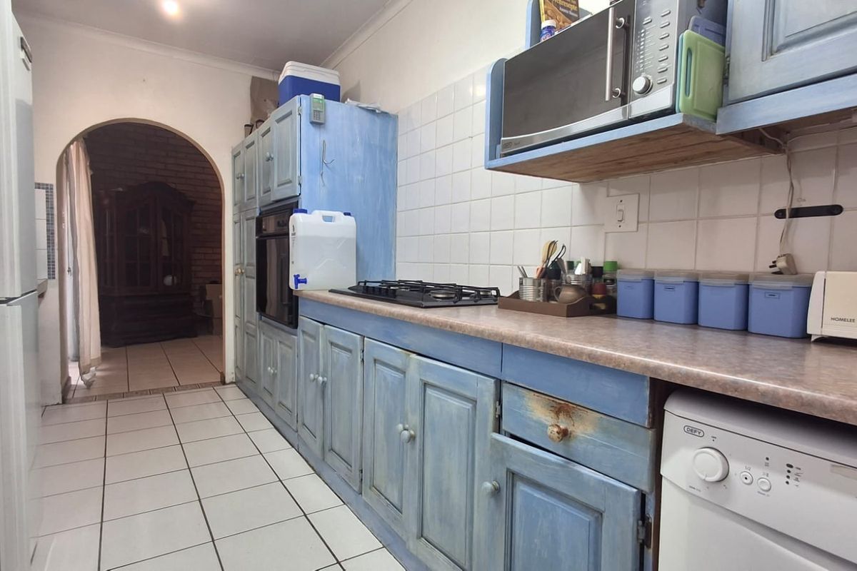 A dated kitchen featuring blue painted cabinetry, laminate countertops, a gas hob, and built-in oven, with tiled flooring and an arched doorway.