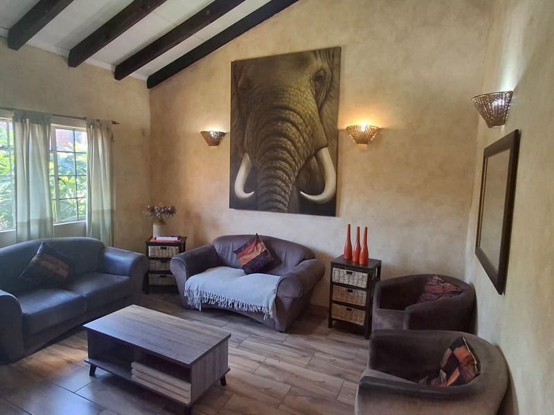 A cozy living room featuring high vaulted ceilings with exposed timber beams, warm textured wall finishes, and tiled flooring.